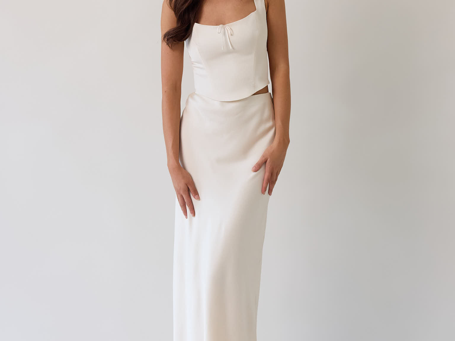 This is the Conrad Set in Ivory. This is a two piece satin set with a fitted, corseted top with thick straps and a delicate tie at the bust and a slight basque waist. It comes with a floor length satin column skirt.