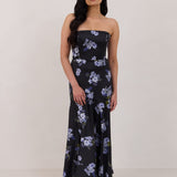A woman is wearing a dark blue strapless dress with a light blue floral print. The dress is fitted in the bodice and hip then flows into a fuller skirt. The dress is tea-length. This is the Sterling Dress in Viola.