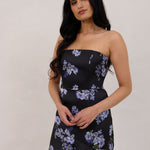 A woman is wearing a dark blue strapless dress with a light blue floral print. The dress is fitted in the bodice and hip then flows into a fuller skirt. The dress is tea-length. This is the Sterling Dress in Viola.
