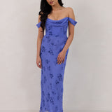 A woman standing against a white background wearing a periwinkle blue floral print dress. The dress has a scooped neckline with an off-the-shoulder strap, is fitted through the bodice and falls to ankle length. The fabric is chiffon. This is the Sutton Dress in Livia.