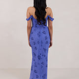A woman standing facing the back against a white background wearing a periwinkle blue floral print dress. The dress has a scooped neckline with an off-the-shoulder strap, is fitted through the bodice and falls to ankle length. The fabric is chiffon. This is the Sutton Dress in Livia.