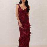 Model wearing the Majorca Dress in Garnet. A full length flowy guesting dress with a deep v neckline and ruffle details. Garnet is a dark red floral print.