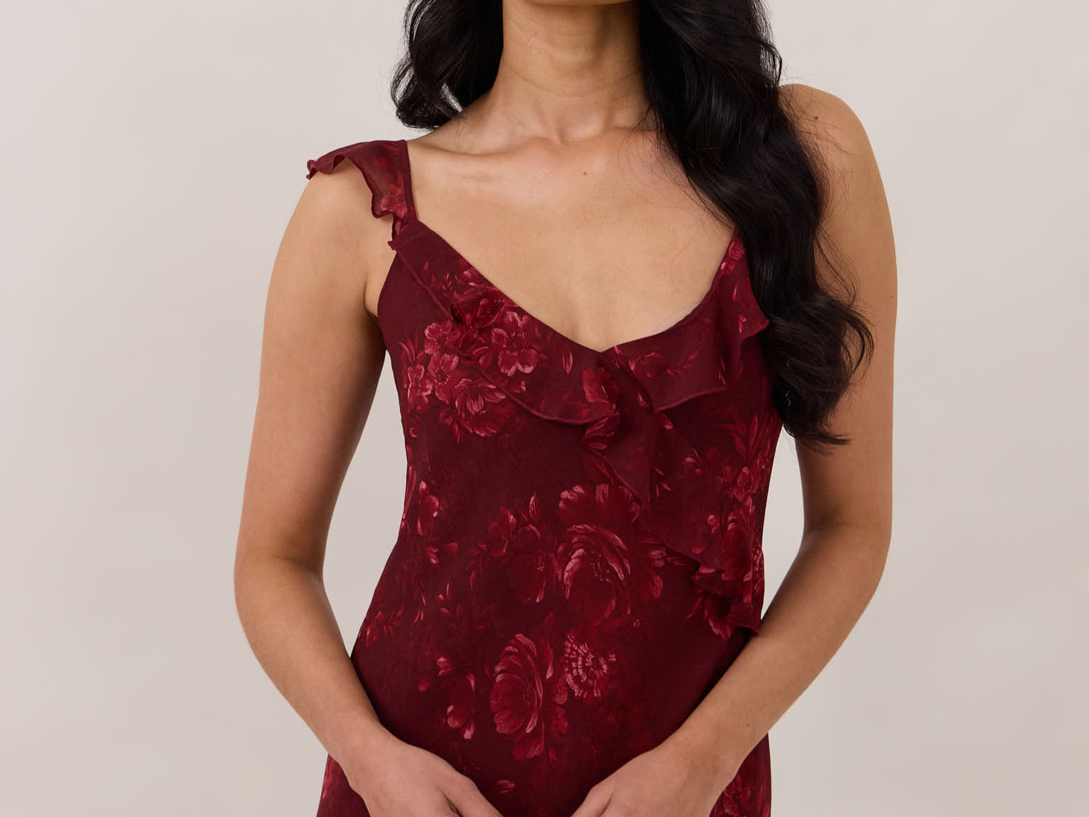 Close up of model wearing the Majorca Dress in Garnet. A full length flowy guesting dress with a deep v neckline and ruffle details. Garnet is a dark red floral print.