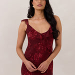 Close up of model wearing the Majorca Dress in Garnet. A full length flowy guesting dress with a deep v neckline and ruffle details. Garnet is a dark red floral print.