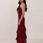 Side shot of model wearing the Majorca Dress in Garnet. A full length flowy guesting dress with a deep v neckline and ruffle details. Garnet is a dark red floral print.
