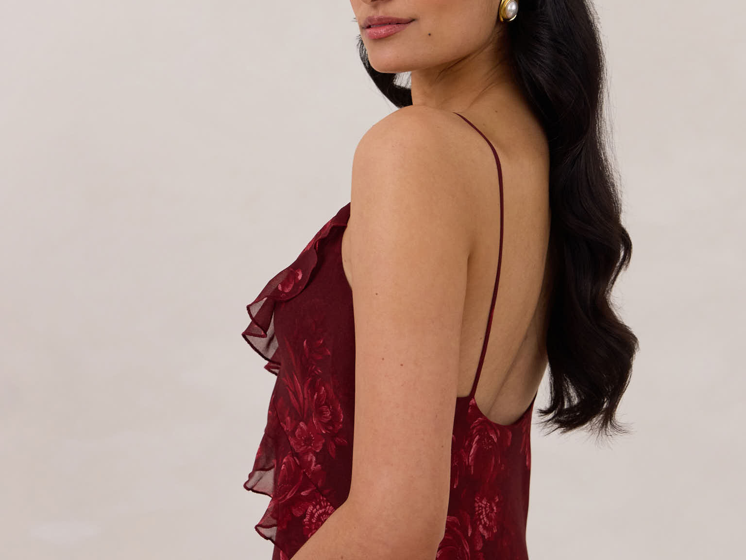 Side shot of model wearing the Majorca Dress in Garnet. A full length flowy guesting dress with a deep v neckline and ruffle details. Garnet is a dark red floral print.