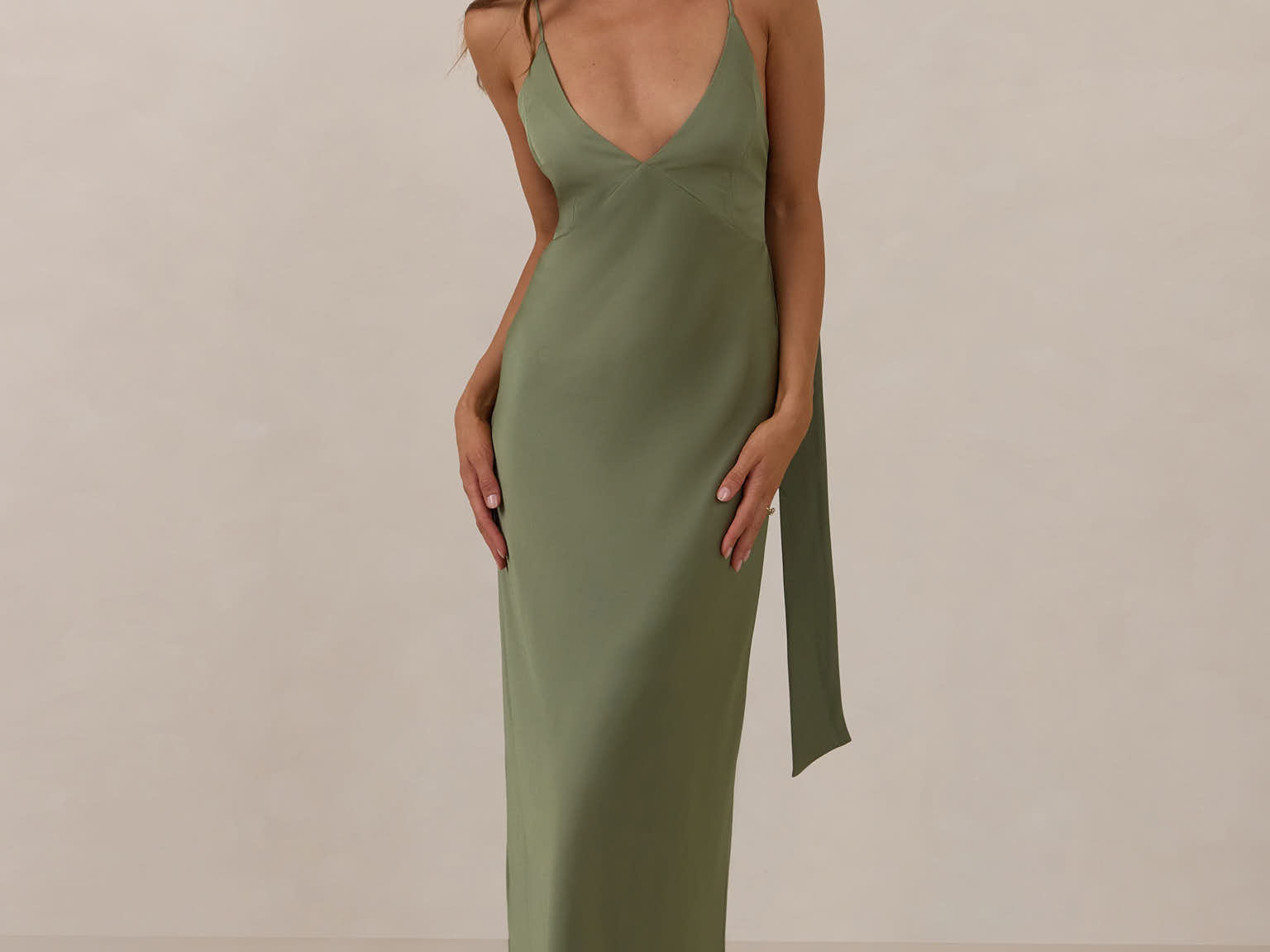 Woman wearing a olive coloured, deep V neck dress against a plain background