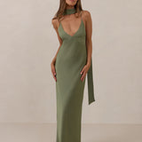 Woman wearing a olive coloured, deep V neck dress against a plain background
