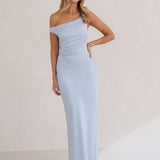 A woman stands infront of a white back drop wearing a powder blue bridesmaid dress. This dress has an asymmetrical neckline and gathers slightly at the waist. Perfect as a bridesmaid dress or a special event dress. This is the Savannah Dress in Powder Blue.