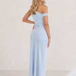 A woman stands infront of a white back drop facing the right wearing a powder blue bridesmaid dress. This dress has an asymmetrical neckline and gathers slightly at the waist. Perfect as a bridesmaid dress or a special event dress. This is the Savannah Dress in Powder Blue.