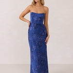 A woman stands against a white backdrop. She's wearing an indigo blue strapless dress with a blue floral print. The dress is fitted through the bodice, and falls nicely over the hips and is tea-length. This is the Brodie Dress in Azure. 