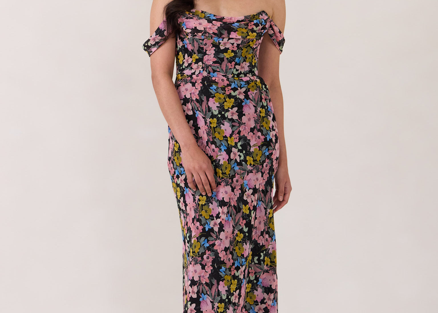 A woman is standing in front of a white background. She's wearing a bold pink and blue floral print strapless dress with an off-the-shoulder strap. This dress is Sutton in Liora and is perfect as a wedding guest dress, or for any special event. 