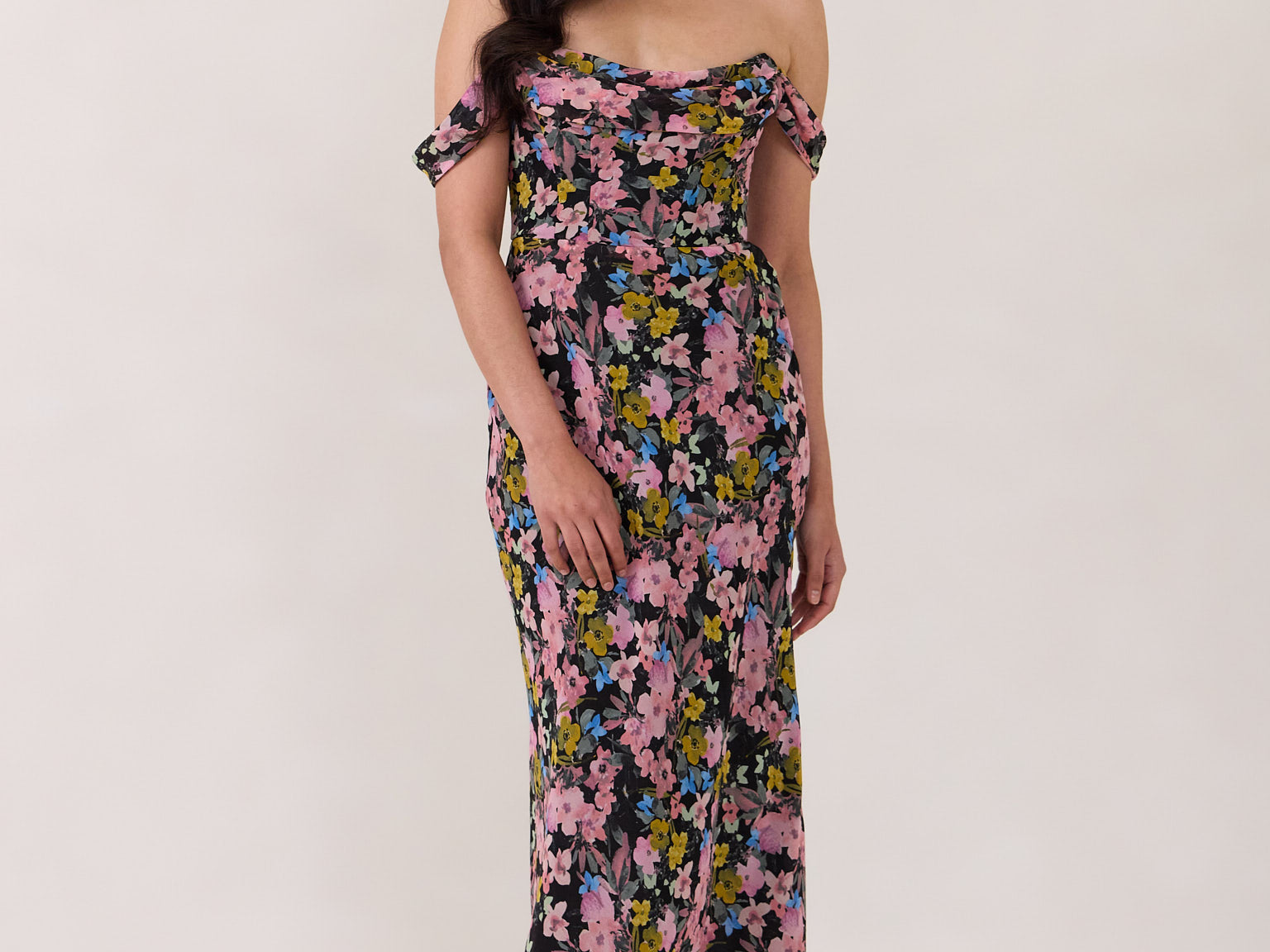 A woman is standing in front of a white background. She's wearing a bold pink and blue floral print strapless dress with an off-the-shoulder strap. This dress is Sutton in Liora and is perfect as a wedding guest dress, or for any special event. 