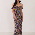 A woman is standing in front of a white background. She's wearing a bold pink and blue floral print strapless dress with an off-the-shoulder strap. This dress is Sutton in Liora and is perfect as a wedding guest dress, or for any special event. 