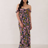 A woman is standing in front of a white background. She's wearing a bold pink and blue floral print strapless dress with an off-the-shoulder strap. This dress is Sutton in Liora and is perfect as a wedding guest dress, or for any special event. 