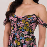 A woman is standing in front of a white background. She's wearing a bold pink and blue floral print strapless dress with an off-the-shoulder strap. This dress is Sutton in Liora and is perfect as a wedding guest dress, or for any special event. 