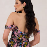 A woman is standing in front of a white background facing the back. She's wearing a bold pink and blue floral print strapless dress with an off-the-shoulder strap. This dress is Sutton in Liora and is perfect as a wedding guest dress, or for any special event. 