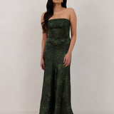 A woman standing against a white backdrop wearing a strapless tea length dress. The dress is a dark green with a subtle green floral print. The dress is fitted through the bodice, and has a more flowy skirt. This is the Sterling dress in Fern.