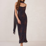 Woman wearing a navy and orange floral chiffon dress with a chiffon scarf on a white background.