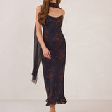 Woman wearing a navy and orange floral chiffon dress with a chiffon scarf on a white background.