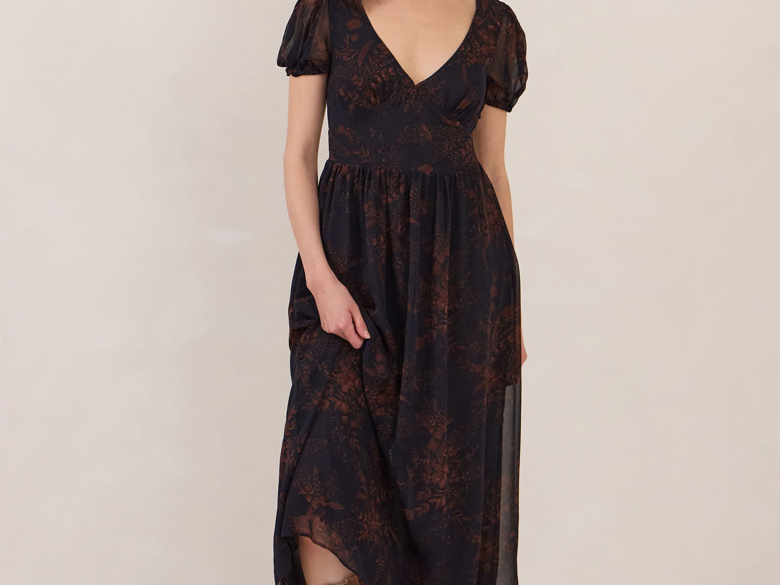 Woman s wearing a dark blue and copper floral print chiffon dress with a v neckline, a slight puffed sleeve and a full skirt. 