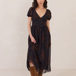 Woman s wearing a dark blue and copper floral print chiffon dress with a v neckline, a slight puffed sleeve and a full skirt. 