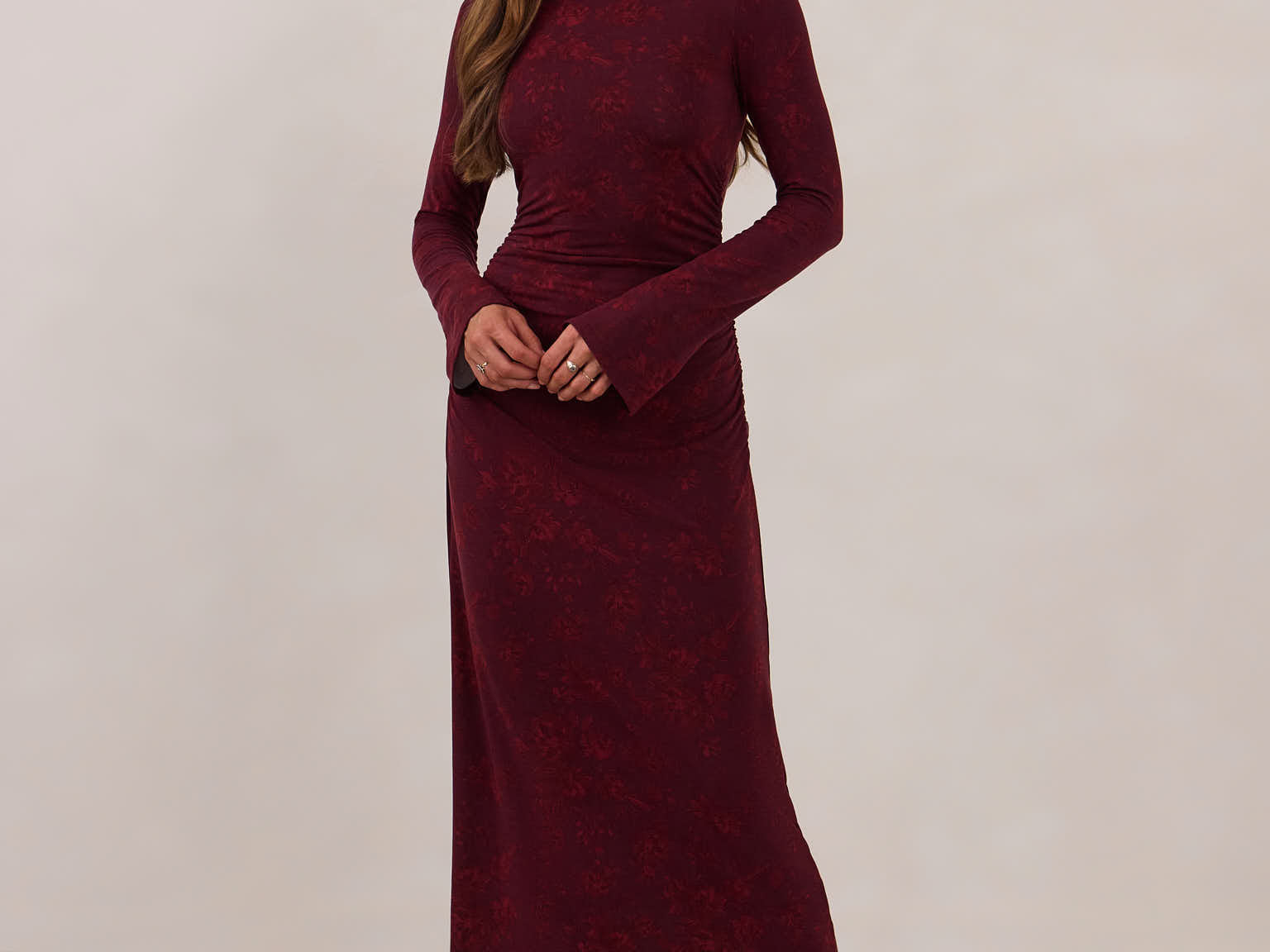 Woman wearing a burgundy dress with long sleeves against a white background