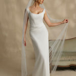 Woman in a white wedding dress with a long veil against a neutral background