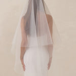 Bride wearing a white wedding dress with a fingertip length veil against a plain background