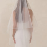 Bride wearing a white wedding dress with a fingertip length veil against a plain background