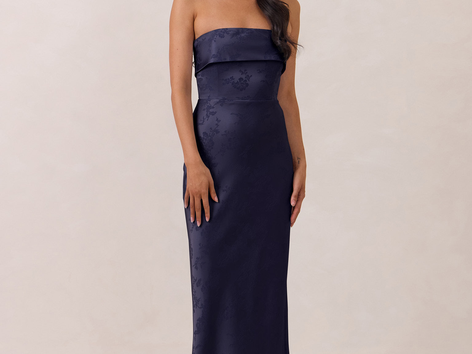 Woman wearing a strapless navy gown against a plain background