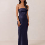 Woman wearing a strapless navy gown against a plain background