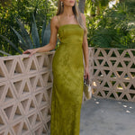 Woman in a green dress standing against a tropical backdrop with palm trees.