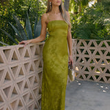 Woman in a green dress standing against a tropical backdrop with palm trees.